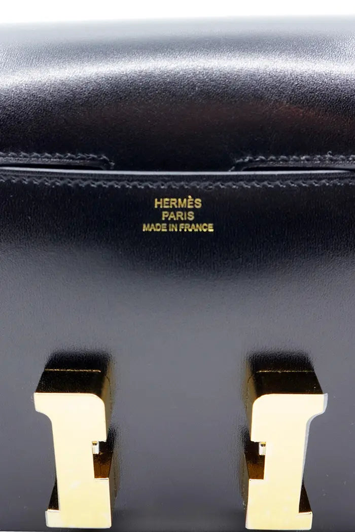 Focus on the Hermès signature, used Constance Box Noir bag.