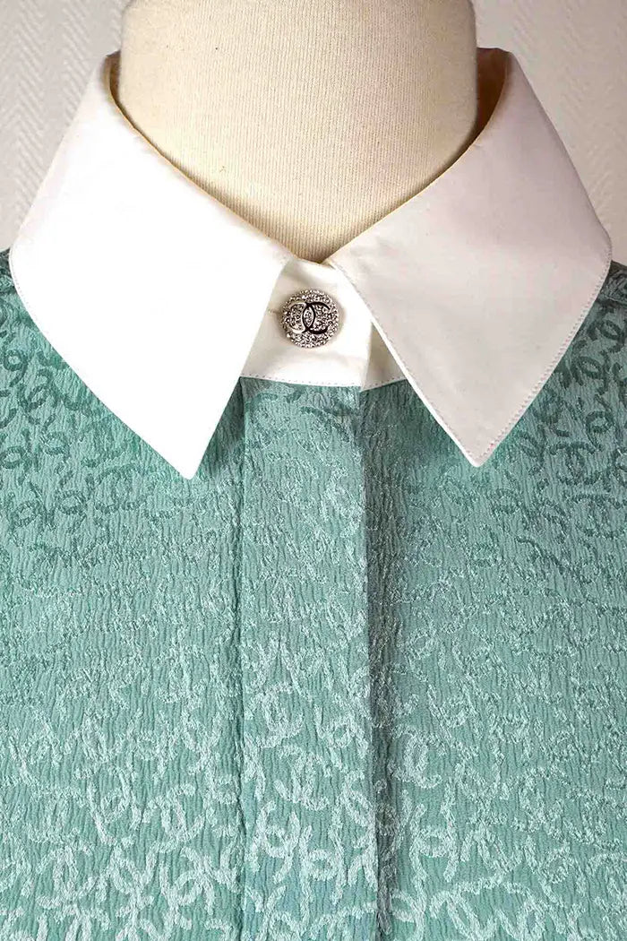 Gros plan sur le col blanc et le bouton brillants à motif CC de la tunique Chanel turquoise preloved