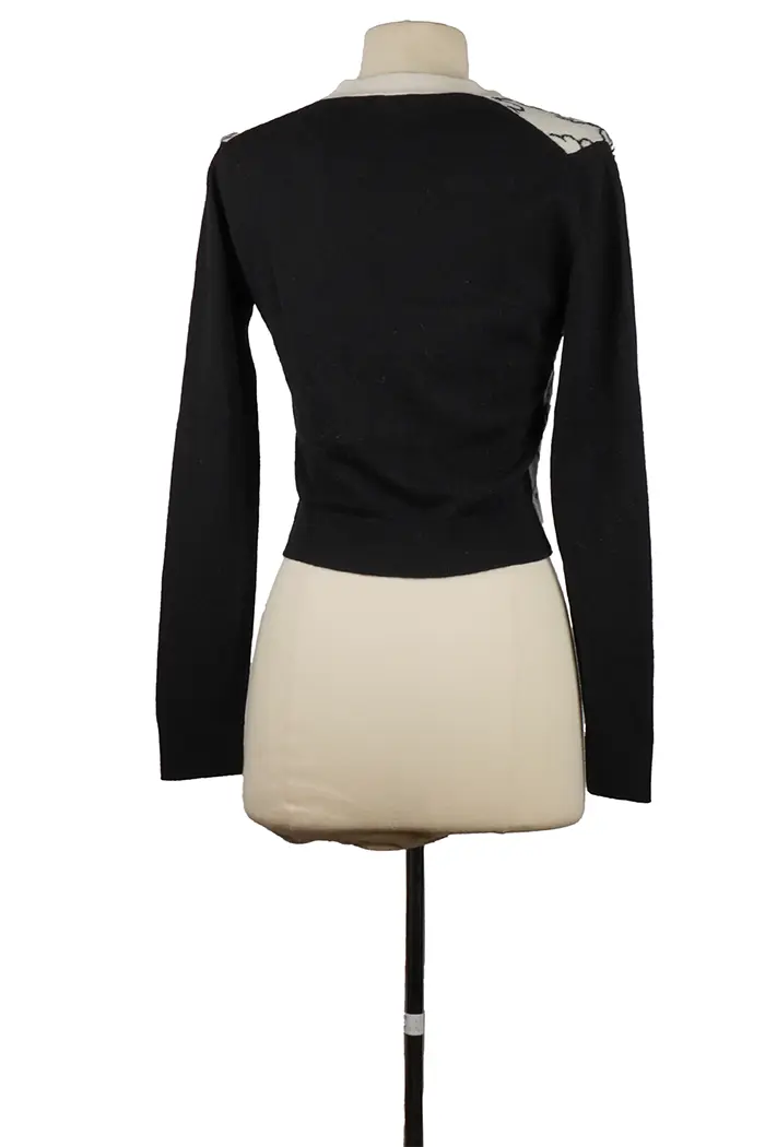 Black back of Chanel cashmere cardigan on mannequin, matching sleeves and straight cut, chic two-tone piece with iconic couture details.