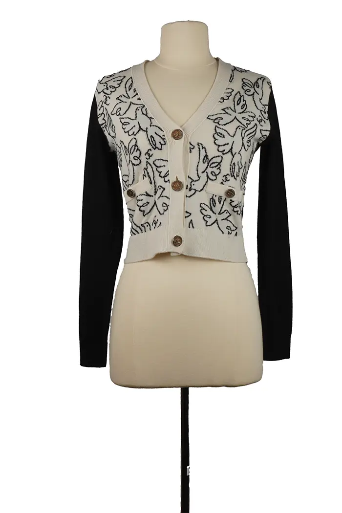 Chanel Croisière 2022 cardigan on mannequin, white cashmere front adorned with black doves, V-neck, gold CC button, black sleeves.