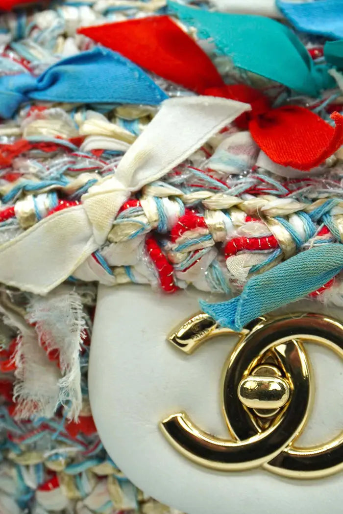 Detail des vergoldeten Verschlusses Classic Flap Chanel, umgeben von Stickereien aus Bast, Seide und Tüll in himmelblauen, grünen und roten Tönen.
