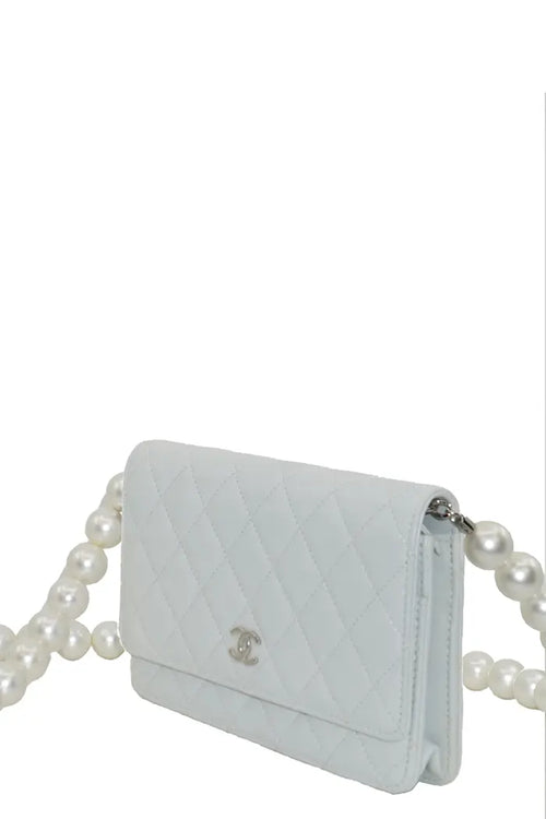 Dreiviertelansicht der blaugrauen Chanel WOC-Tasche, eine kostbare Silhouette, die durch die ausgefallene Perlenkette hervorgehoben wird.