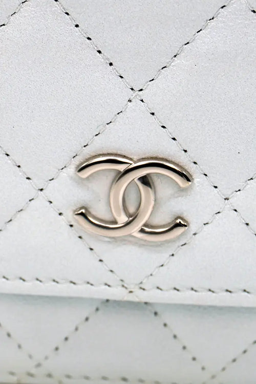 Zoomen Sie auf das geprägte CC-Logo der Chanel WOC-Tasche, dezent und ikonisch auf blaugrauem Lammleder.