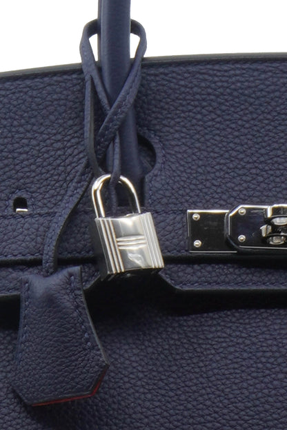 Close-up of padlock, Ref. 1000068. Silver padlock on a navy blue leather of the Birkin bag. Reench preloved.