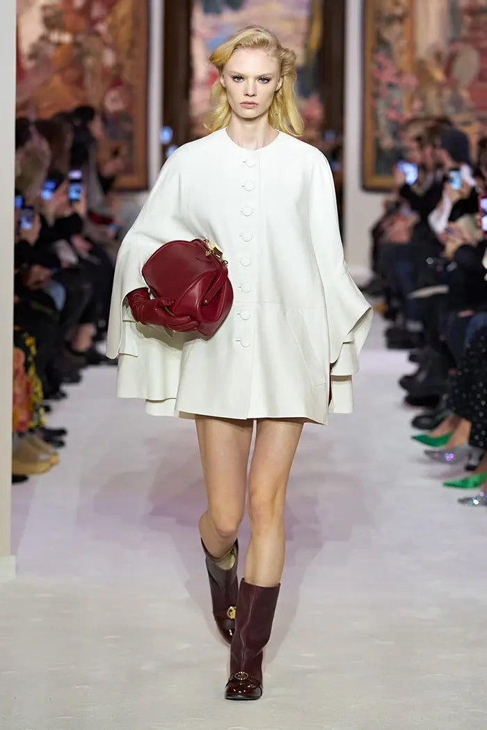 Modelo luciendo una capa Lanvin durante un desfile de moda con un bolso rojo y botas marrones Lanvin