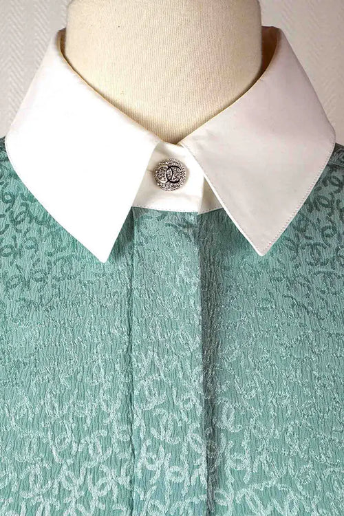 Gros plan sur le col blanc et le bouton brillants à motif CC de la tunique Chanel turquoise preloved