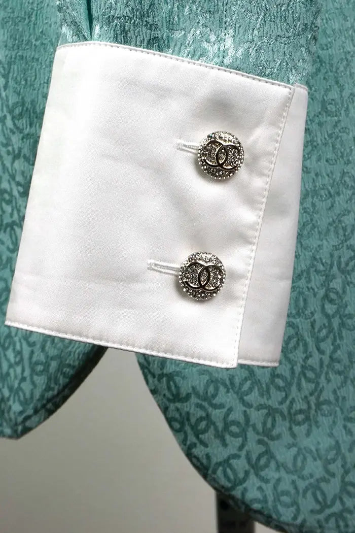 Gros plan sur les boutons brillants à motif CC sur le poignet de la tunique Chanel turquoise.