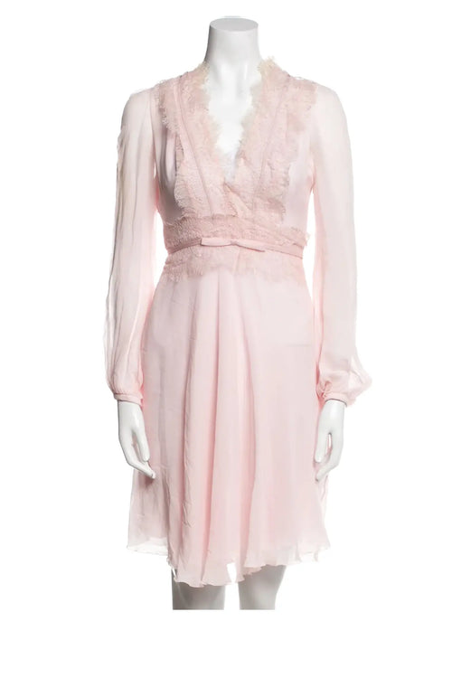 Mini-robe Giambattista Valli en soie rose sur mannequin, coupe A-line, manches longues, encolure en V et détails en dentelle avec nœuds décoratifs.