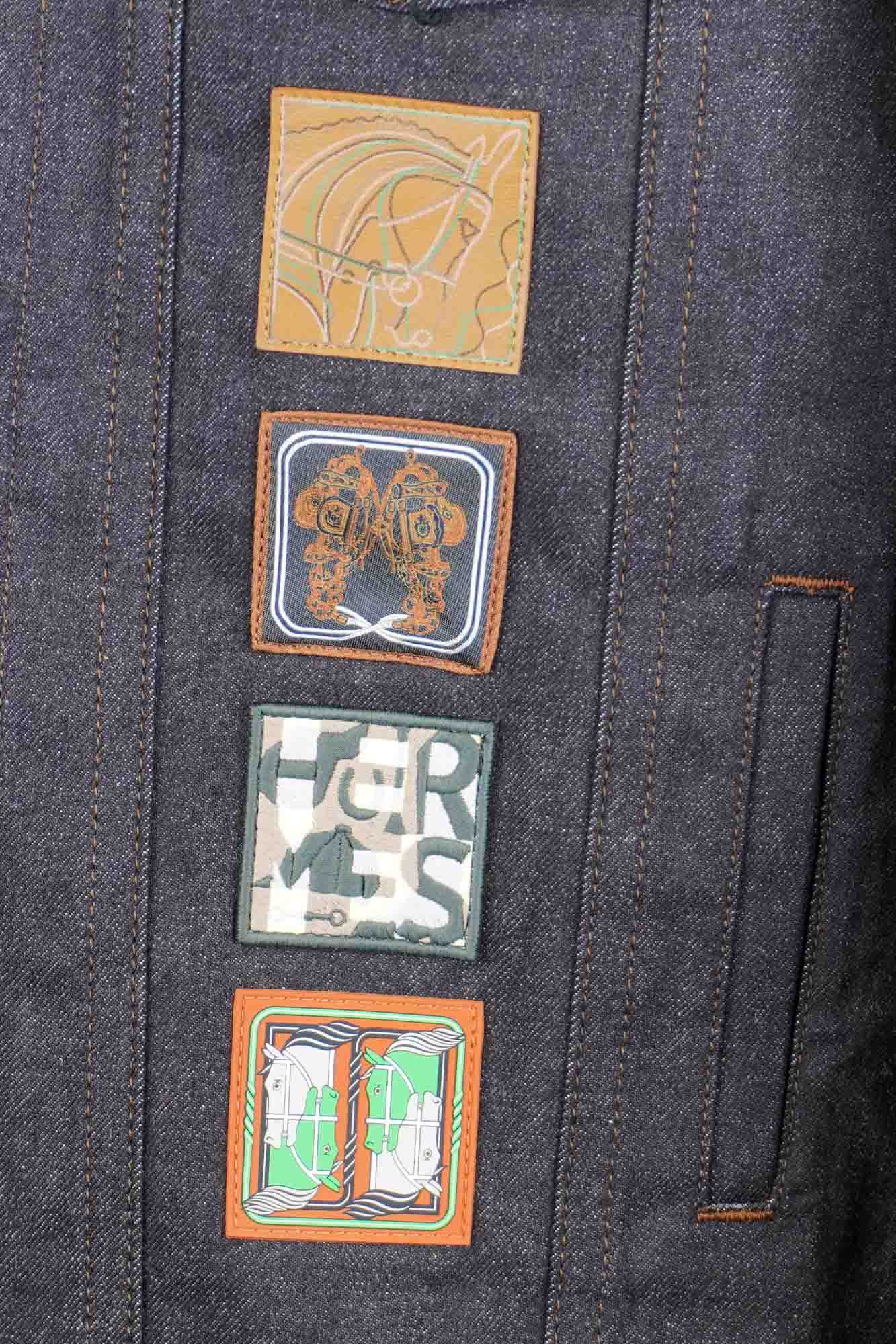 Hermès Icone au Carré denim boyfriend jacket, Size 48, never worn with tags, preloved, certified authentic, eco-friendly fashion. Includes travel garment bag. One-day DHL delivery. | zoom on the badges, front of the jacket